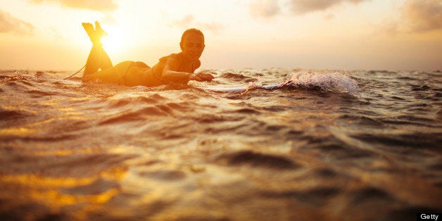 surfer girl paddling in ocean on white surfboard