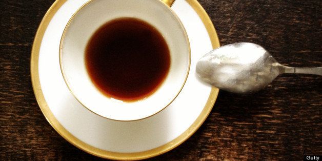 Espresso cup, saucer and spoon from above on a dark wooden surface.