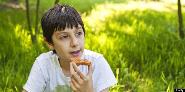 Young Boy Eating Bread and Jam Outdoors in a meadow at sunset