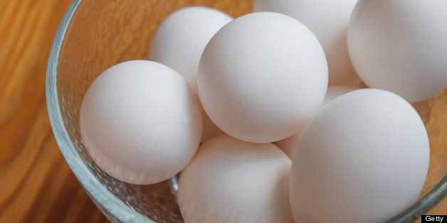 A small bowl filled with eggs on a hardwood counter.