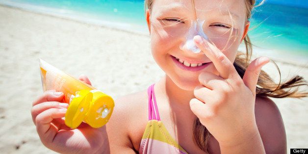 Little girl applying suntan lotion on the beach