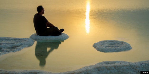 A man sitting and meditating on a salt formation in the dead sea at sunrise.