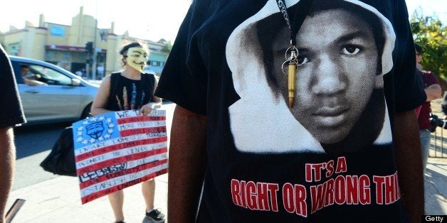 A man wears a single bullet around his neck over his Trayvon t-shirt as people hold placards and shout slogans during a rally in Los Angeles in the aftermath of George Zimmerman's acquittal in the shooting death of Florida teen Trayvon Martin, on July 15, 2013 in California, where local civil rights activists and other leaders urged participants to remain peaceful as they express frustration with the trial's outcome. AFP PHOTO/Frederic J. BROWN (Photo credit should read FREDERIC J. BROWN/AFP/Getty Images)