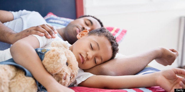 Father and son with stuffed toy sleeping in bed