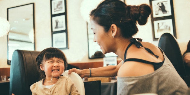 Pretty young mom and toddler having fun playing on the dining table in a restaurant joyfully.