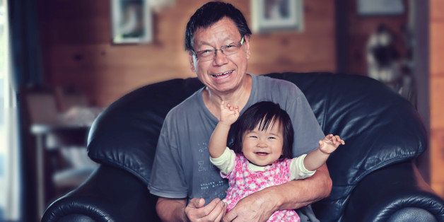 Eleven months old Chinese baby girl sitting on grandfather's lap. They are both happy and laughing.
