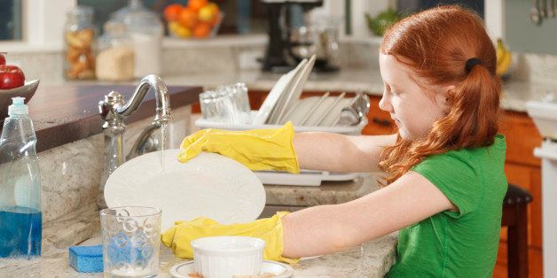 little redhead girl cheerfully washing dishes at home in kitchen