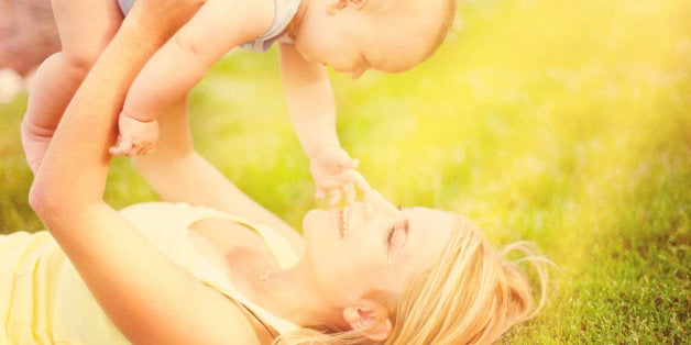 Mother and baby son lying down in grass bathing in sunrays
