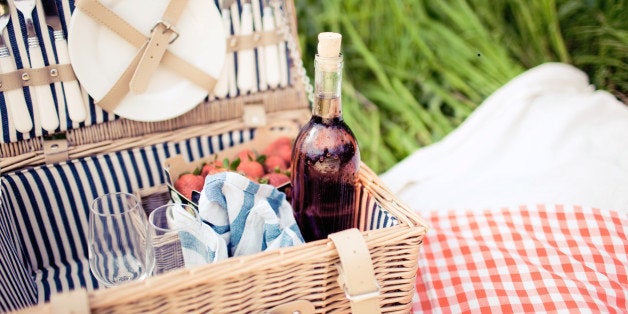 Picnic basket with rose, glasses, strawberries and dishes in meadow.