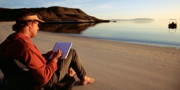 Man sitting on beach writing in journal.