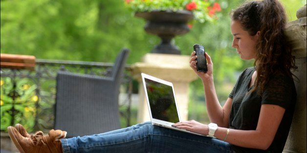 BRUSSELS , BELGIUM - JUNE 25, 2013: A young woman uses a mobile phone and laptop on June 25, 2013 in Brussels, Belgium. (Picture by Didier Lebrun/Photonews via Getty Images)