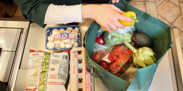 A woman puts groceries into a reusable grocery bag in the bagging area of the checkout line. 