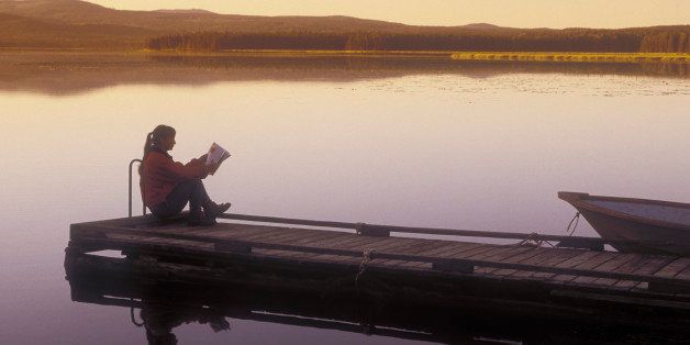 woman reading on wharf at dusk on spout Lake in front of Ten-ee-ah Lodge in the Cariboo region of British Columbia, Canada.
