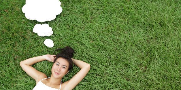 Young Asian woman with thought bubbles lying on meadow smiling.