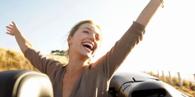 Young Woman Sits in the Back of a Convertible, Her Arms in the Air, Laughing With Joy