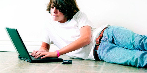 Teenage boy laying on floor working on laptop computer with cell by his side . (Photo by: Universal Education/Universal Images Group via Getty Images)