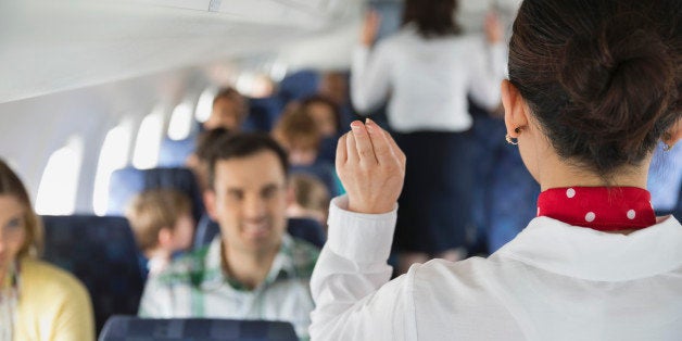 Rear view of flight attendant indicating exits to passengers in airplane