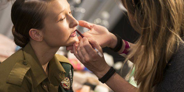 A make-up artists applies make-up to a model wearing her military service uniform before she changed backstage to walk down the catwalk during the Tel Aviv Fashion Week, on March 11, 2014 in the Mediterranean coastal city of Tel Aviv. AFP PHOTO / JACK GUEZ (Photo credit should read JACK GUEZ/AFP/Getty Images)