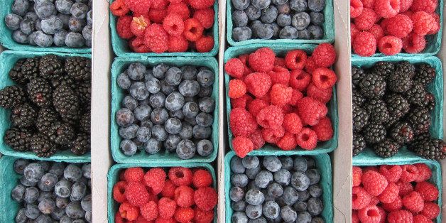 Overhead view of alternating baskets of blueberries, raspberries, and blackberries on display at local farmers market.