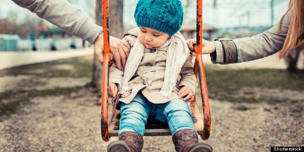 Sad child on a swing, in-between her divorced parents holding her separately.