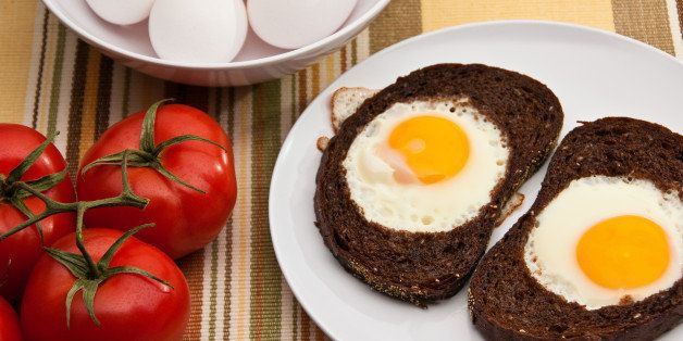 Eggs sunny side up in a slice of bread accompanied by bowl of eggs and tomatoes