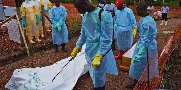 Sierra Leonese government burial team members disinfect the body bag of an Ebola victim at the Medecins Sans Frontieres (MSF) facility in Kailahun, on August 14, 2014. Kailahun along with the Kenema district is at the epicentre of the worst epidemic of Ebola since its discovery four decades ago. The death toll stands at more than 1,000. The Ebola epidemic in West Africa claimed a fourth victim in Nigeria on August 14 while the United States ordered the evacuation of diplomats' families from Sierra Leone and analysts warned of a heavy economic toll on the stricken region. AFP PHOTO/Carl de Souza (Photo credit should read CARL DE SOUZA/AFP/Getty Images)