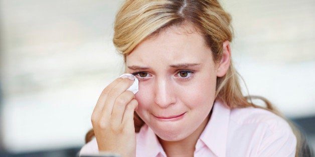 An emotional young woman wiping her tears away while reading a text message