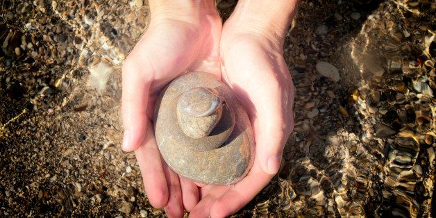 Stones balanced in cupped hands over shallow sea