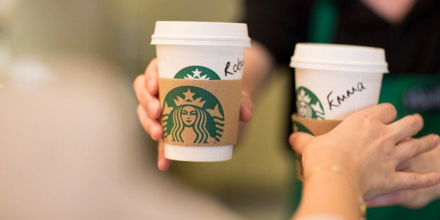 An employee, right, hands a customer personalised cardboard coffee cups inside a Starbucks Corp. coffee shop in London, U.K., on Monday, June 9, 2014. U.K. services companies' confidence rose to a record this quarter, indicating continued expansion in the largest part of the economy, the Confederation of British Industry said. Photographer: Jason Alden/Bloomberg via Getty Images