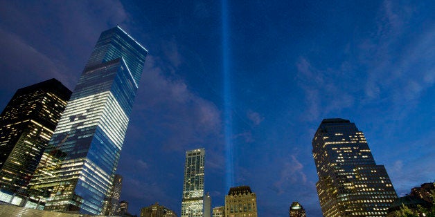 In this Monday, Sept. 8, 2014 photo, the Tribute in Light rises behind buildings adjacent to the World Trade Center in New York. The art installation consists of 88 searchlights aiming skyward in two columns, in memory of the former twin towers. Four World Trade Center is at left. Thirteen years after 9/11 forever changed the New York skyline, officials say developments at the World Trade Center are on track and on budget. (AP Photo/Mark Lennihan)