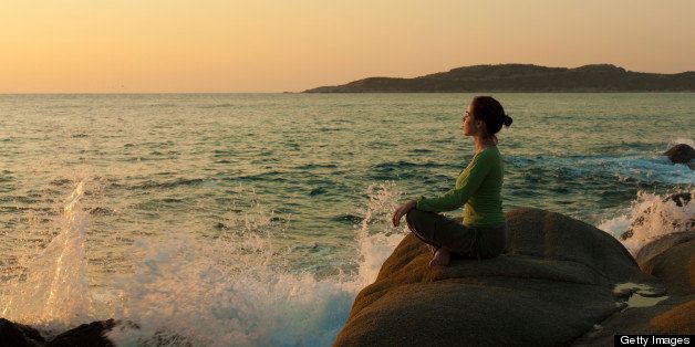 Woman practicing yoga near the sea at sunrise
