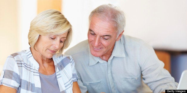Happy senior couple budgeting their monthly expenses using calculator at home