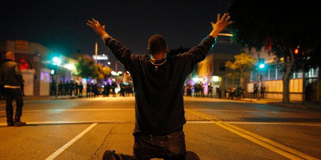 LOS ANGELES, CA - NOVEMBER 25: A man kneels in the street before a line of police officers about to charge at protesters reacting to the grand jury decision not to indict a white police officer who had shot dead an unarmed black teenager in Ferguson, Missouri, in the early morning hours of November 25, 2014 in Los Angeles, California. Police officer Darren Wilson shot 18-year-old Michael Brown on August 9, sparking large ongoing protests. (Photo by David McNew/Getty Images)