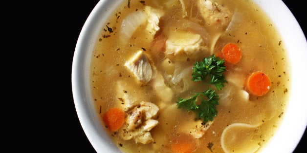 Homemade chicken soup in white bowl against black background.