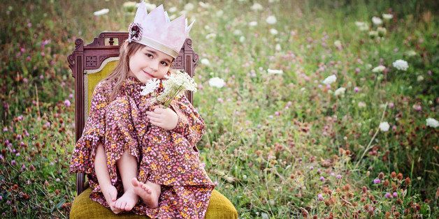 Little girl with princess crown sitting on chair in field.