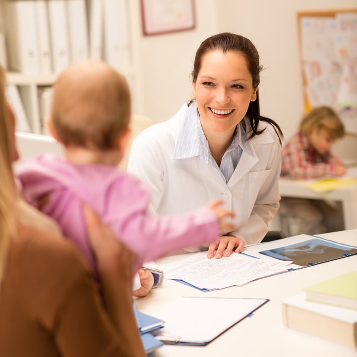 Female pediatrician smiling at baby patient sitting behind office desk