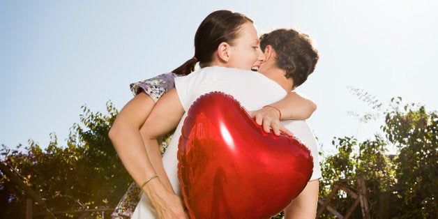 woman grabs heart shaped balloon from man.