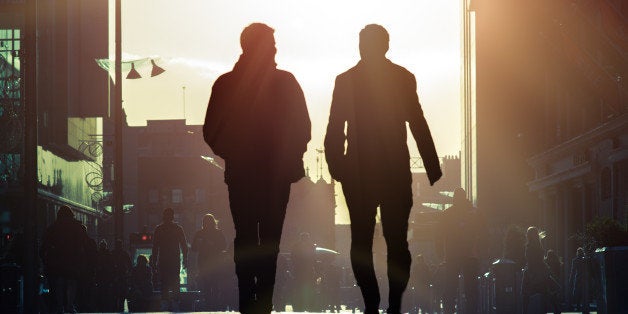 Two men talking and walking down pedestrian street into sunlight.