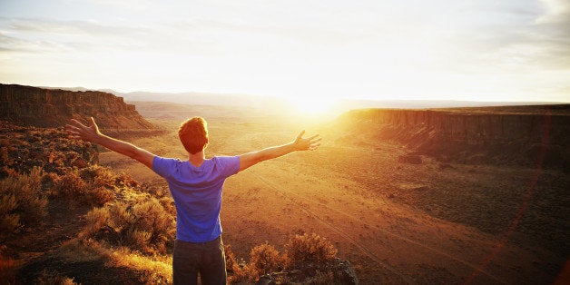 Man standing with arms outstretched looking out at desert canyon at sunset