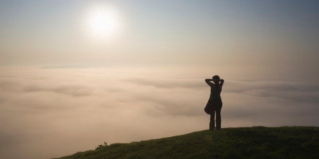 Lone figure on Glastonbury tor looking towards the Isle of Avalon shrouded by mist, Glastonbury, Somerset, England