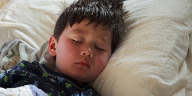 Half Asian Young Boy (3-4 years old) sleeping in bed wearing rocket pajamas with his head on a pillow Dreaming.