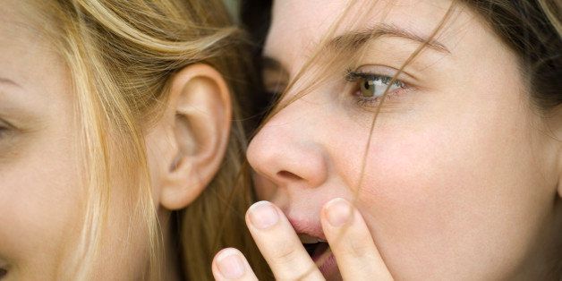 Young woman whispering secret into friend's ear, close-up