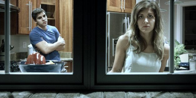 Young couple seen in their upscale kitchen from outside their window, seeming to have a dispute, girl looking out window from kitchen sink