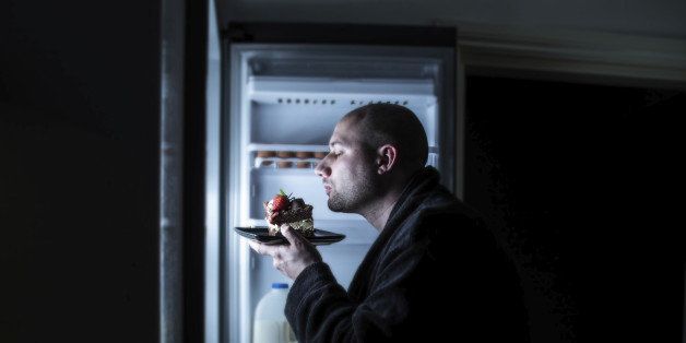 a bald man in his dressing gown sniffing and savouring a slab of cake left in the fridge.
