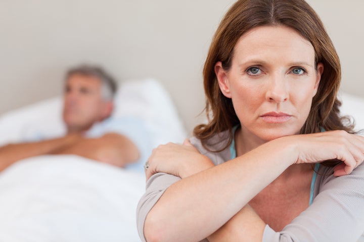 Sad woman on the bed with her husband in the background