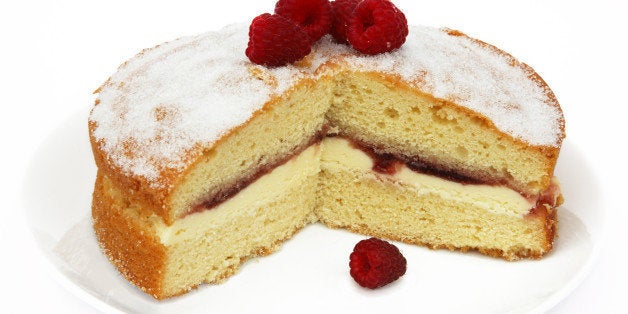 Home made Victoria sponge cake filled with butter cream and raspberry jam, topped with home grown raspberries, on a white plate with white background.