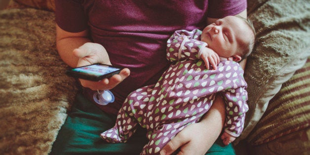 Father using a smart phone while holding his newborn baby daughter