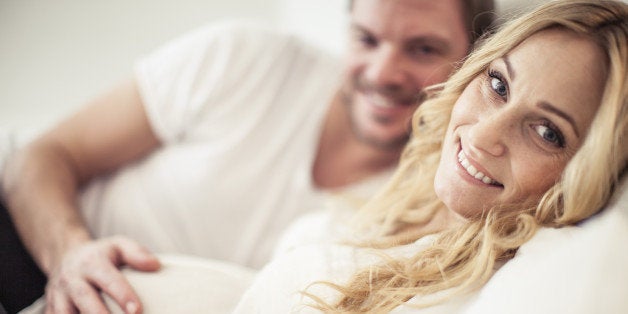 Portrait of happy pregnant woman with man lying in bed