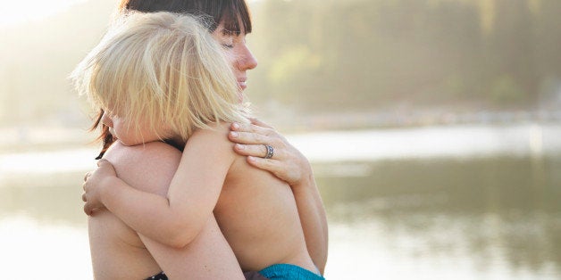 Mother holding son in her arms, standing by lake