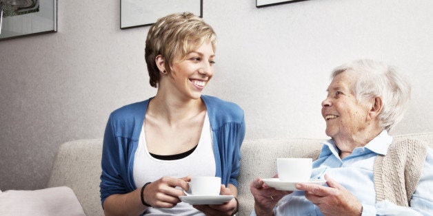 senior woman, 88 years old and caregiver, sitting on sofa, drinking coffee and having a nice conversation